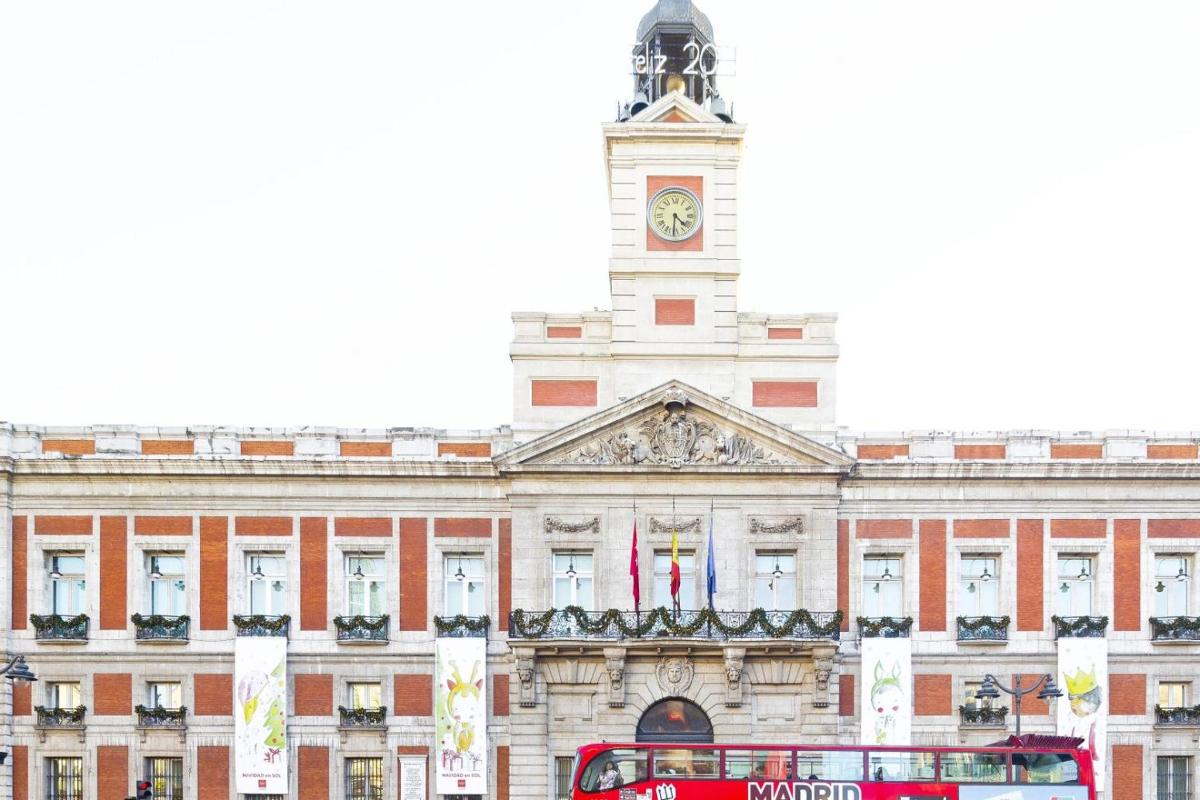 a red bus in front of a building with a clock tower