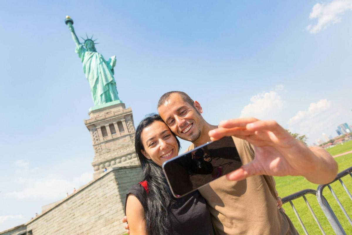 Un hombre y una mujer tomándose una foto frente a la Estatua de la Libertad.