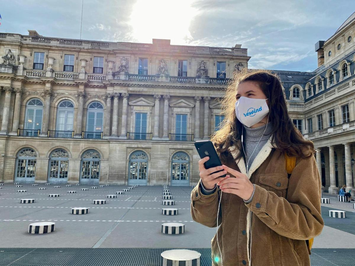 egy maszkot viselő nő, miközben a mobiltelefonját nézi