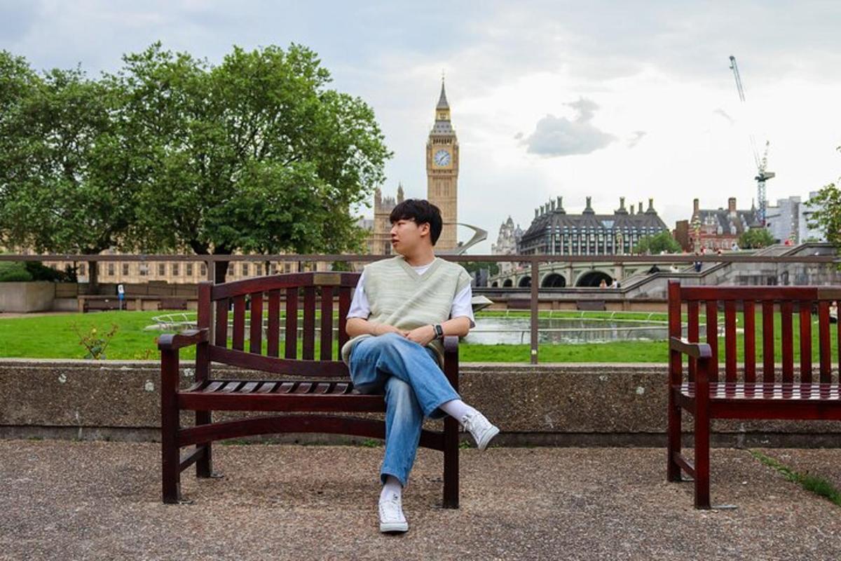 một người đàn ông đang ngồi trên băng ghế công viên với một tháp đồng hồ
