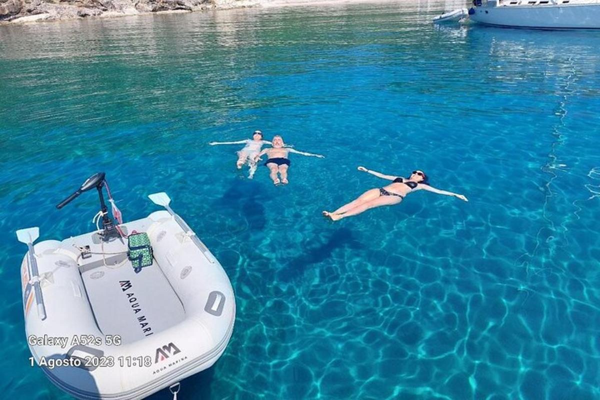 trije ljudje plavajo v vodi poleg čolna
