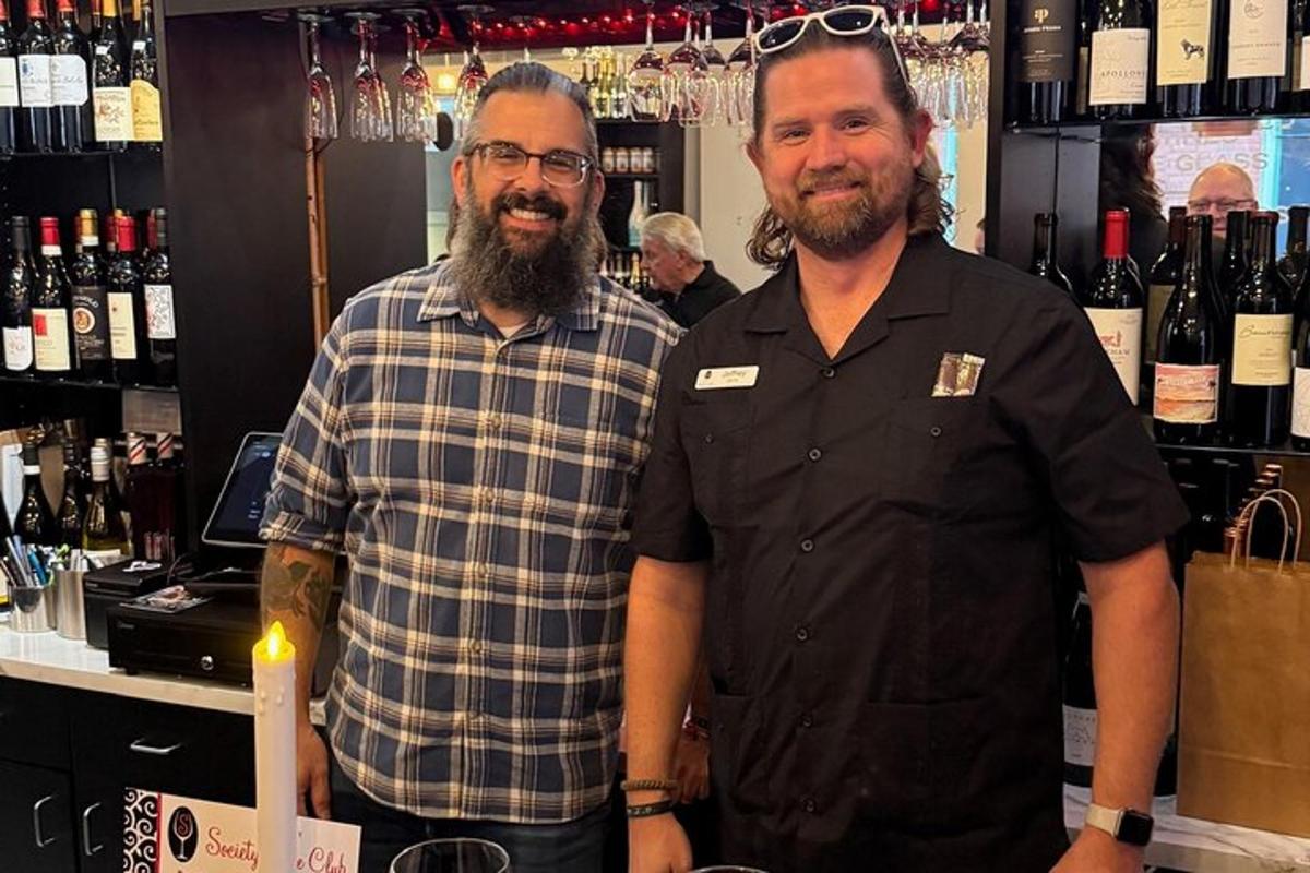 dois homens em pé em frente a um balcão com garrafas de vinho