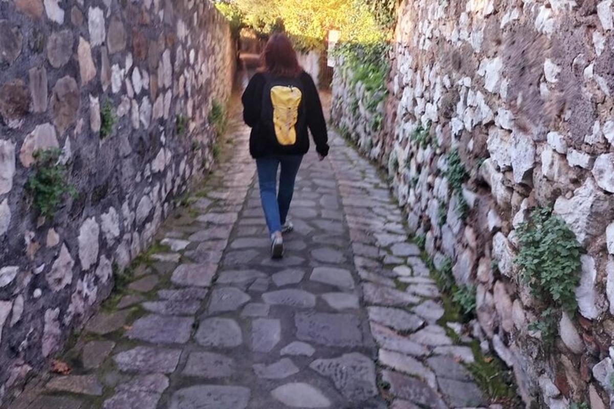 una dona amb una motxilla groga caminant per un carreró de pedra