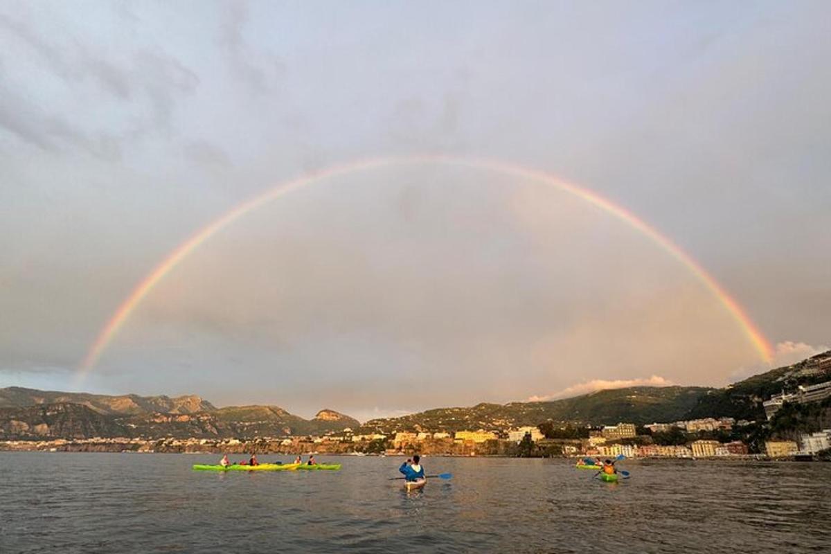 een regenboog boven een watermassa met mensen in kajaks
