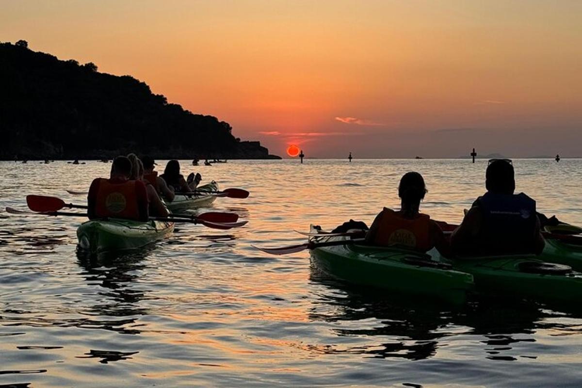 een groep mensen die bij zonsondergang op het water kajakt