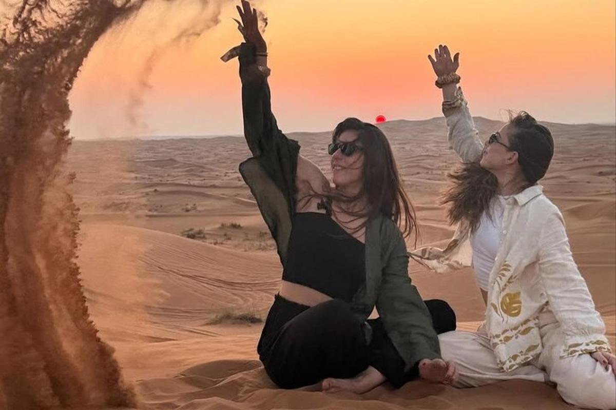 due donne sedute nel deserto con le mani in aria