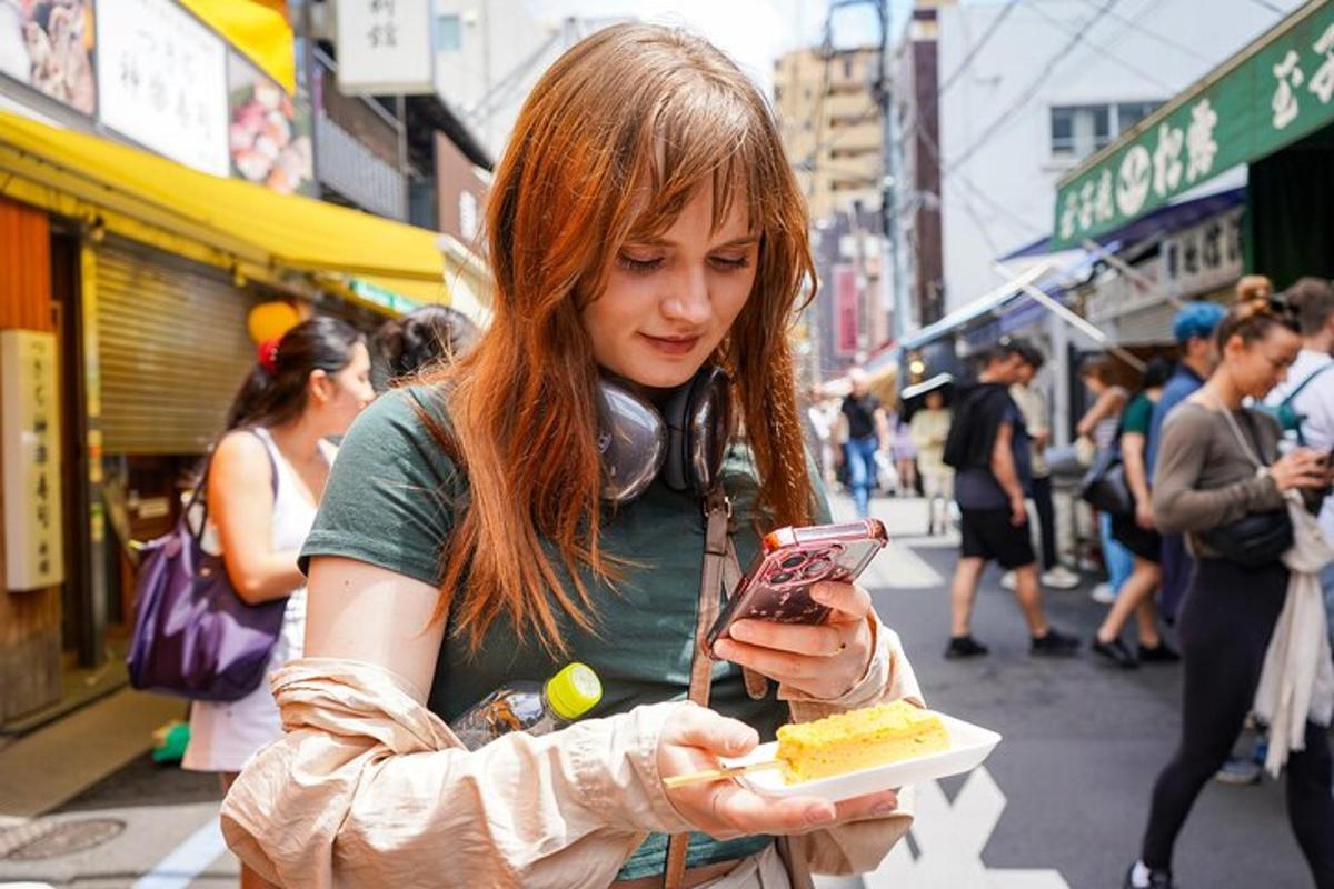 egy nő a mobiltelefonját nézi, miközben egy szelet tortát tart a kezében