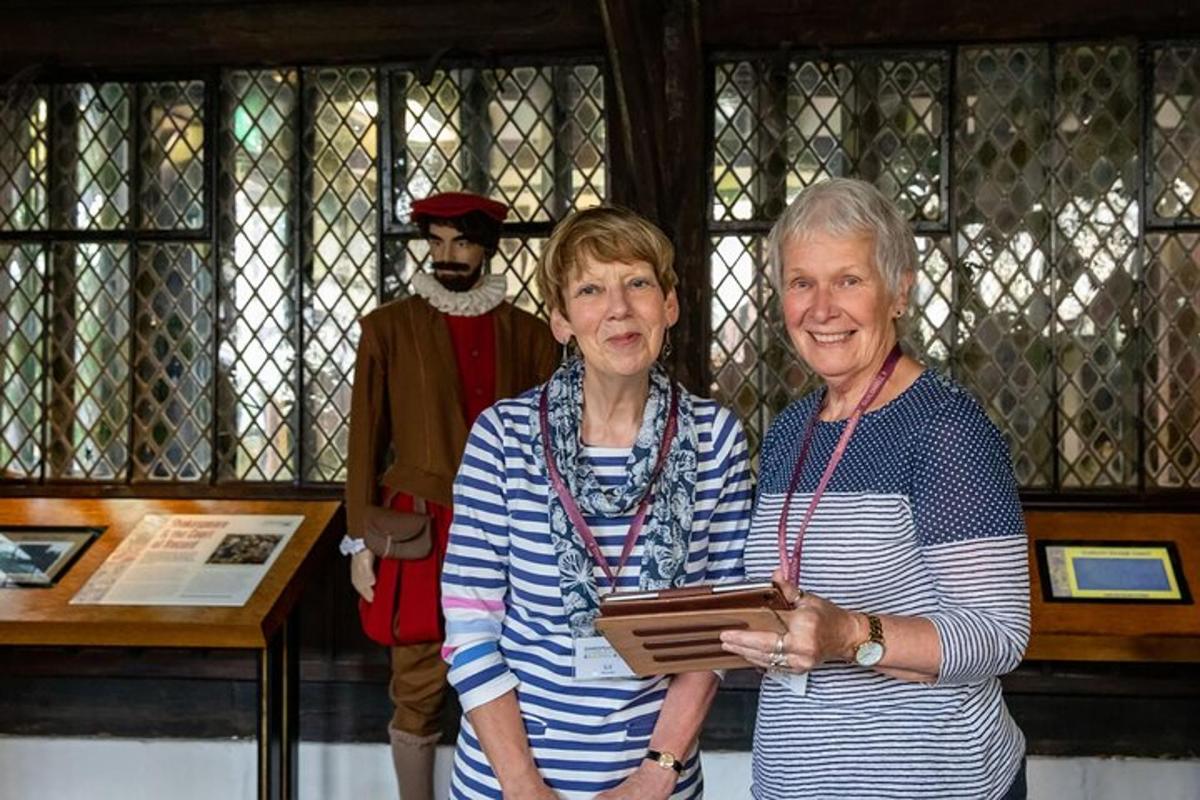 two older women standing next to a statue of a man