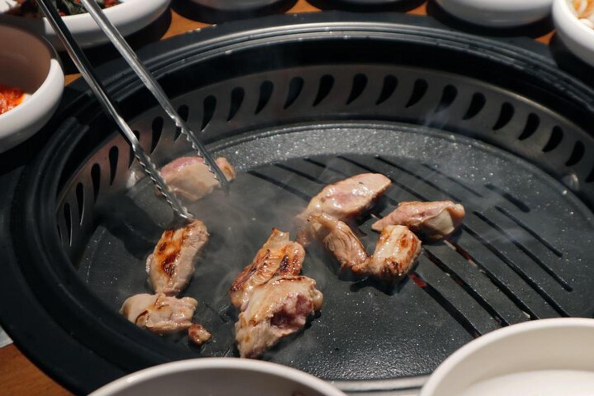ein Haufen Fleisch, das mit einer Zange auf einem Grill zubereitet wird