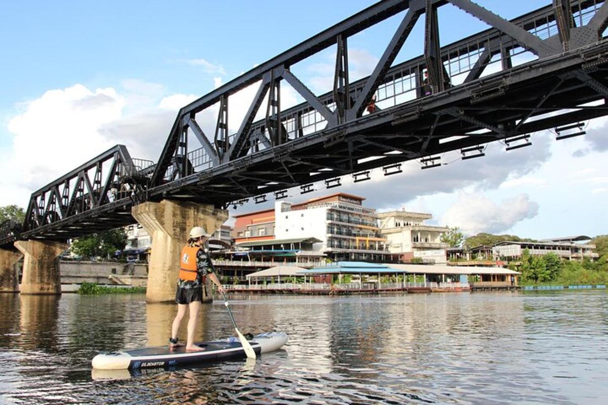 a man on a paddle board in the water under a bridge