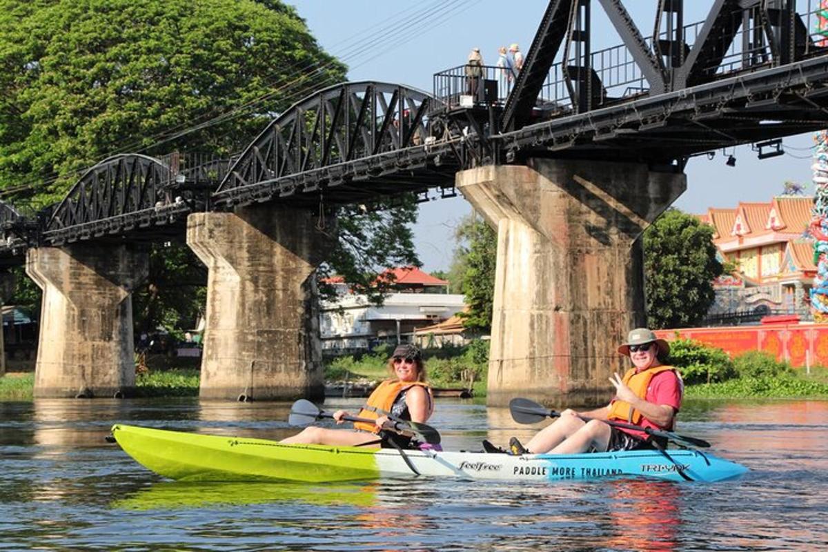 three people in kayaks on the water under a bridge