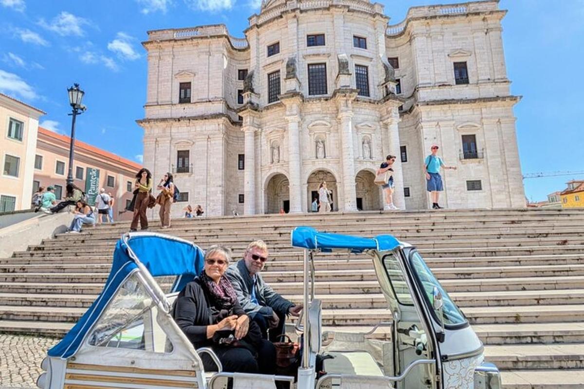 Ένα ζευγάρι που οδηγεί ένα αμαξίδιο του γκολφ μπροστά από ένα κτίριο
