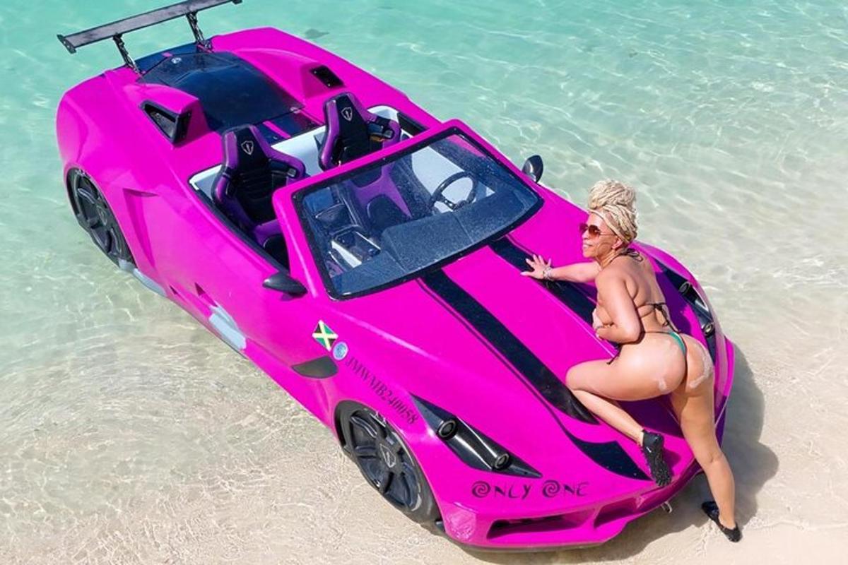 Una mujer sentada en un coche rosa en la playa.