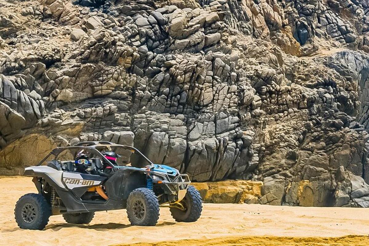 Un vehículo todo terreno estacionado en la arena cerca de una montaña rocosa