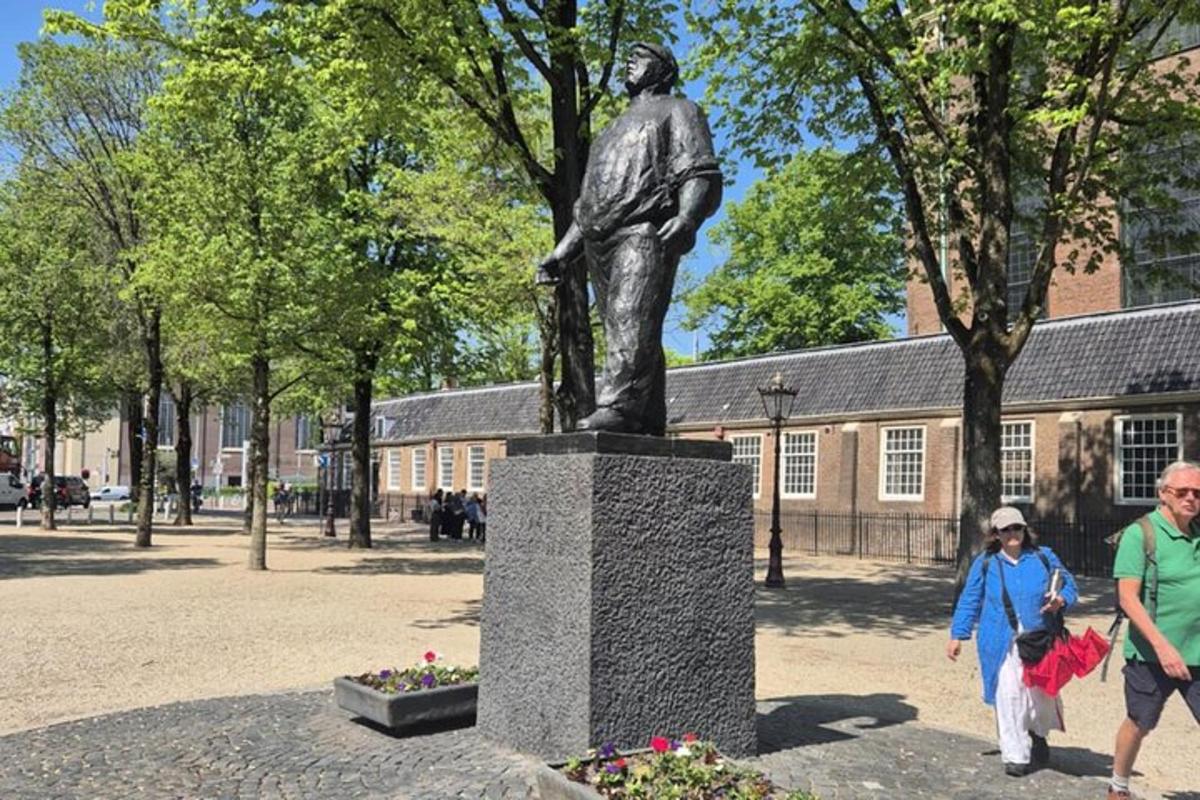 en staty av en man i en park med människor som går förbi