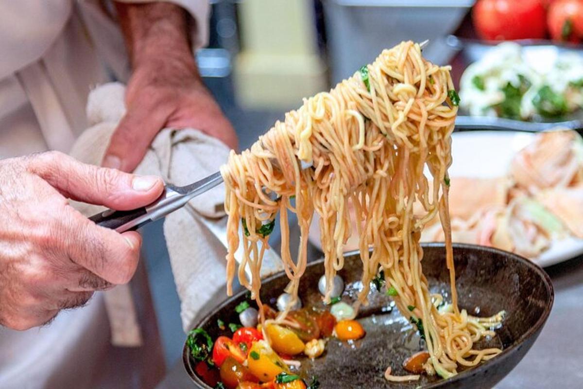 een persoon die een tang vasthoudt en spaghetti eet