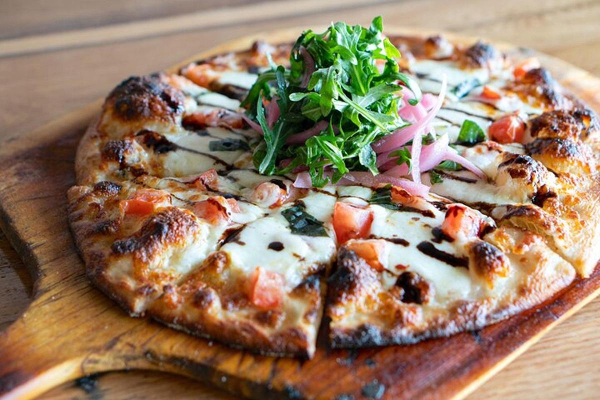 una pizza sobre una taula de tallar de fusta amb una amanida a sobre