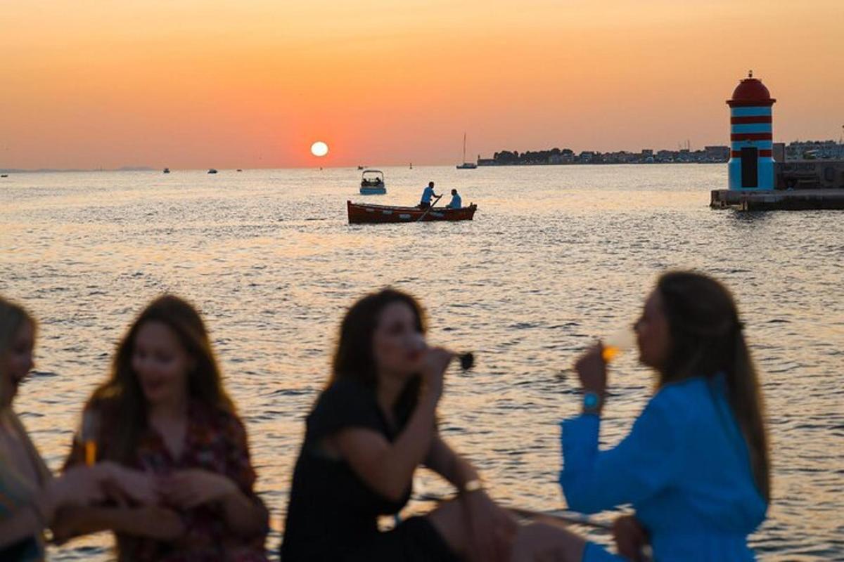 skupina žensk, ki sedijo na plaži in opazujejo sončni zahod