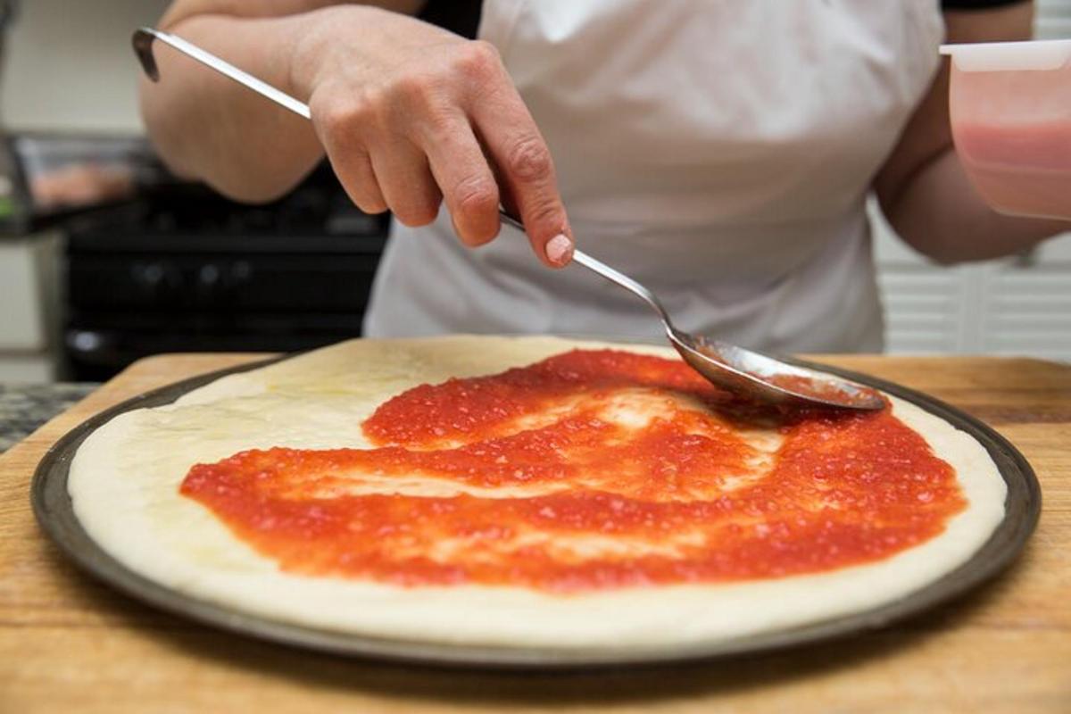 seseorang yang memegang pisau dan garpu di atas pizza