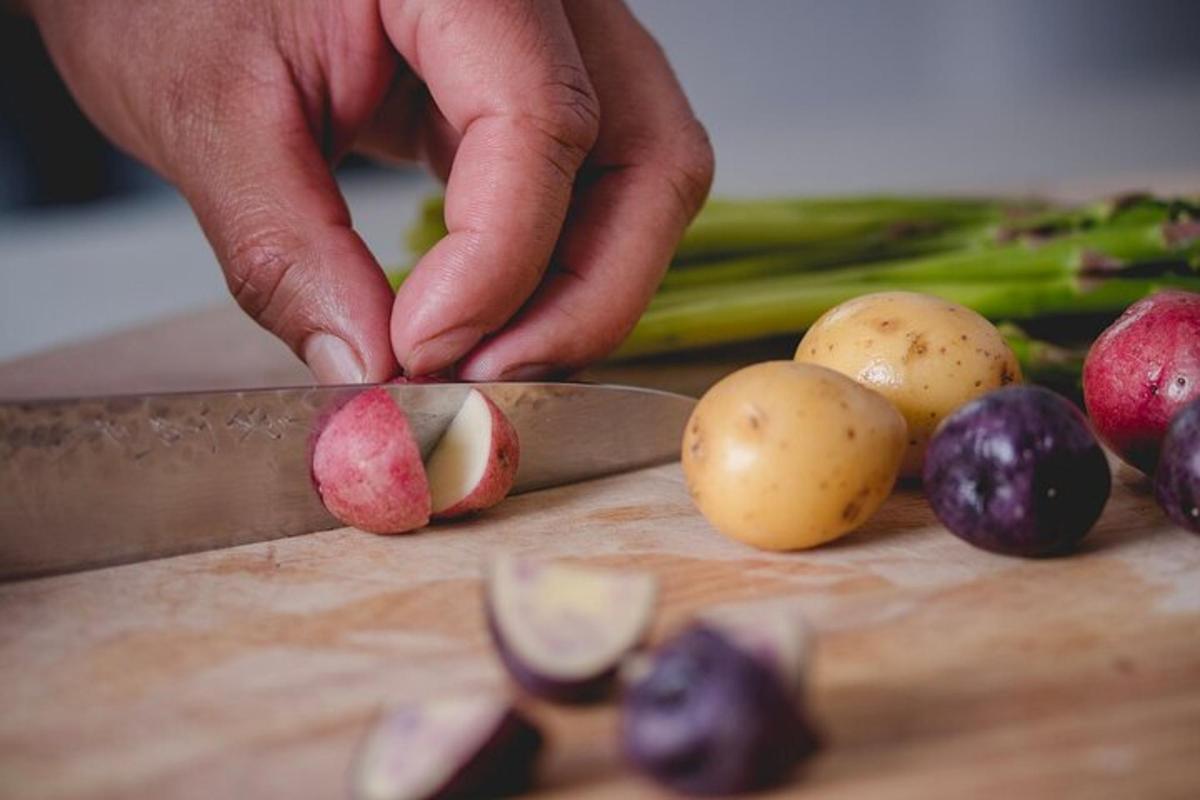 una persona che taglia le patate su un tagliere con le verdure