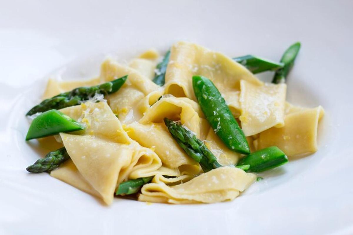 um prato branco de macarrão com aspargos e verduras