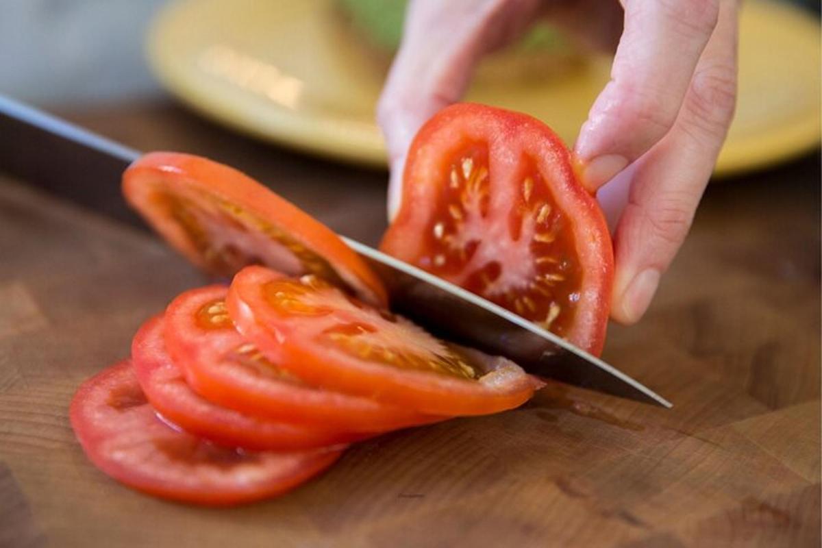 una persona che taglia un pomodoro con un coltello