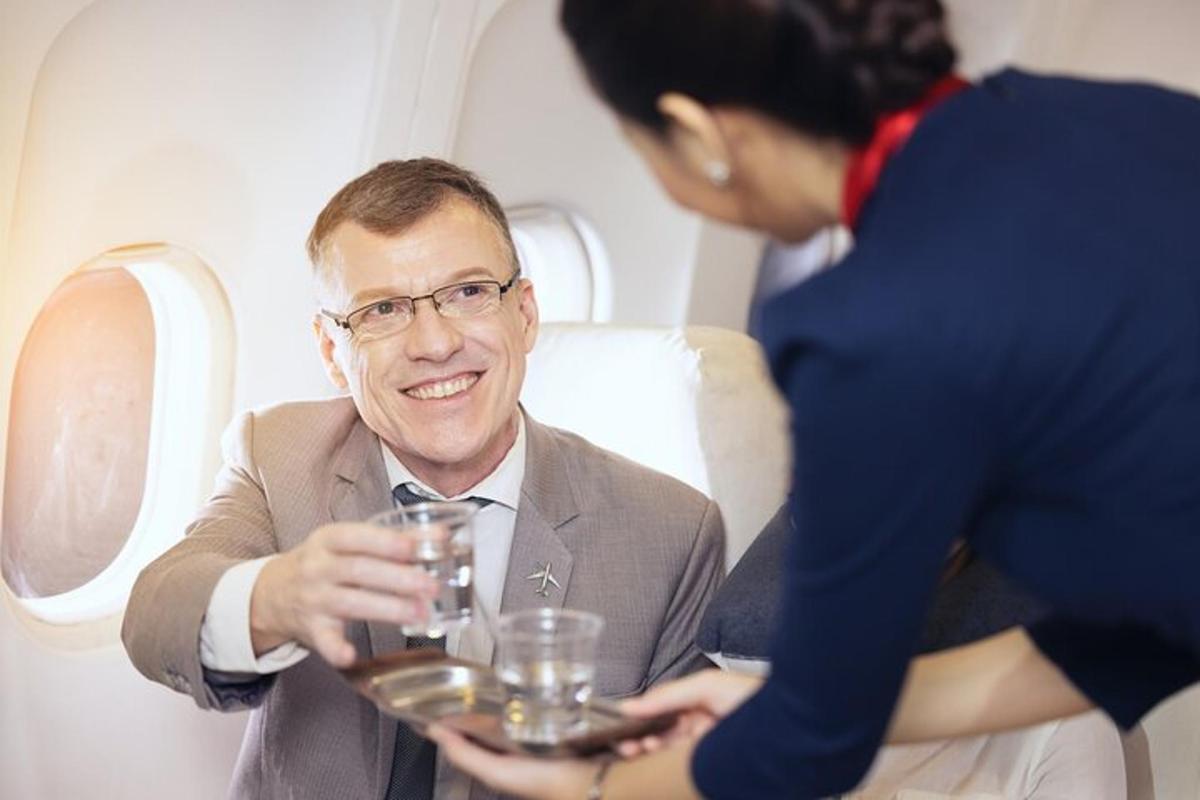 Un hombre sentado en un avión con una mujer sosteniendo un vaso.