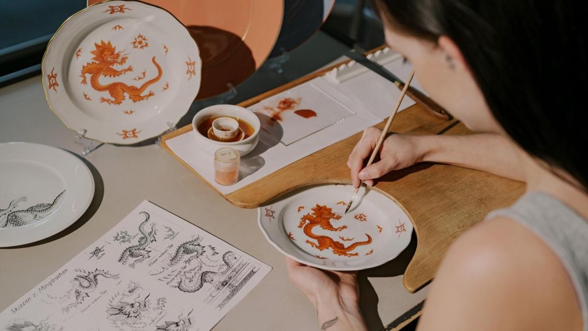 a woman painting a bowl with a dragon on it