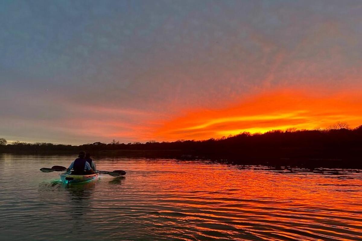 una persona seduta su un kayak in acqua al tramonto