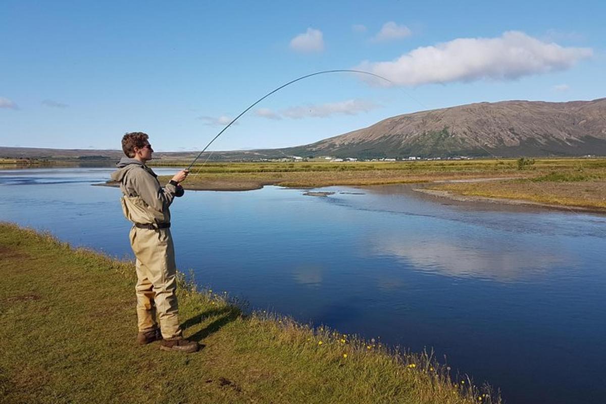 Maður stendur við ána og heldur á veiðistöng