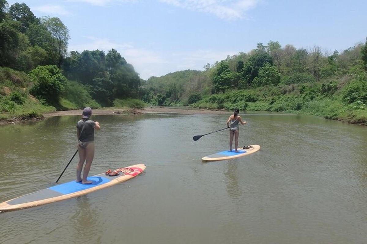 Două persoane stau pe plăci de paddleboard pe un râu