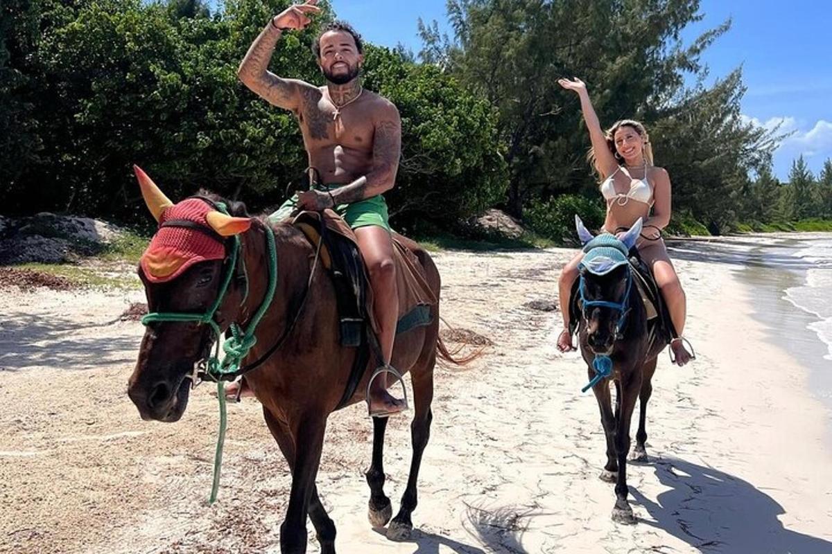 a man and a woman riding horses on the beach