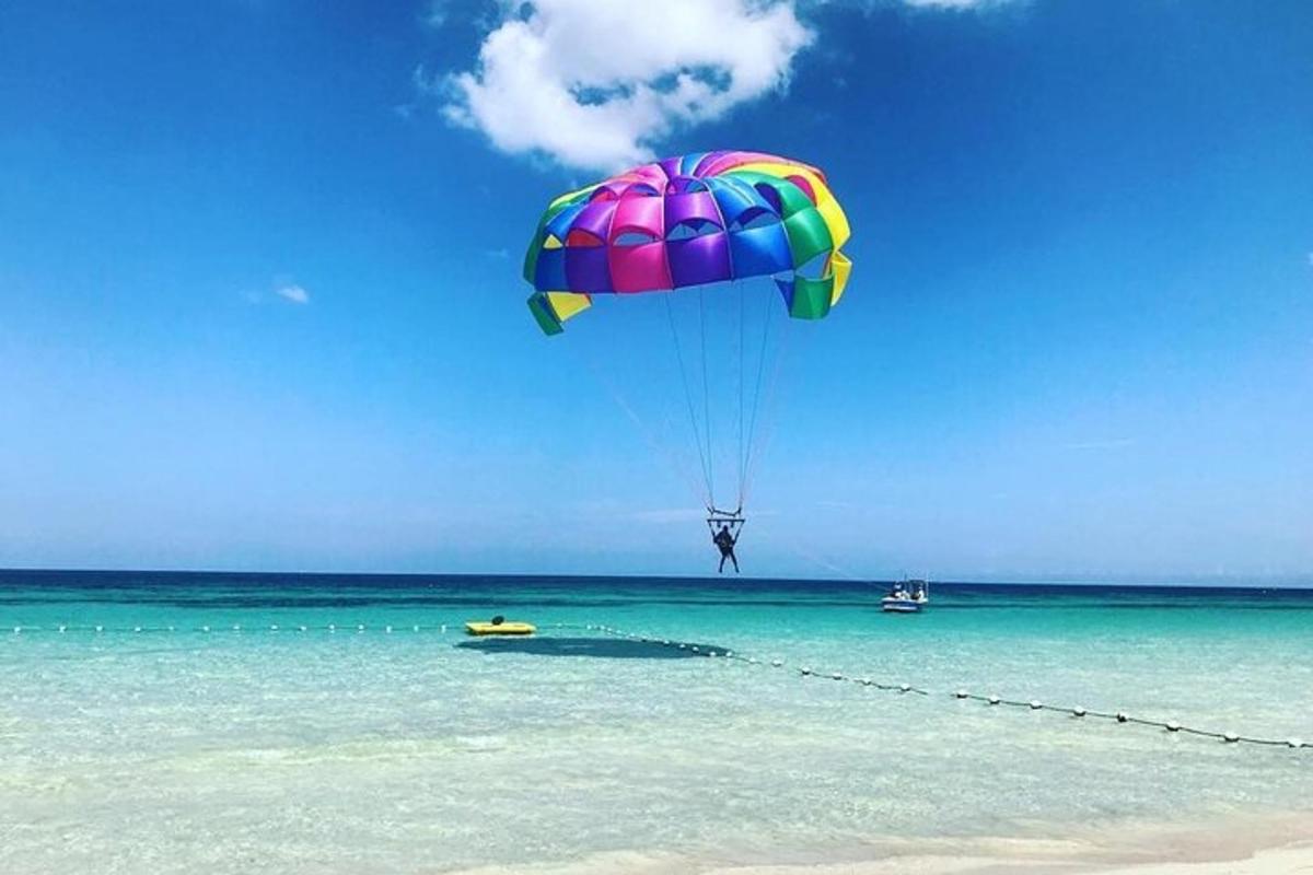uma pessoa voando de paraquedas sobre a água em uma praia