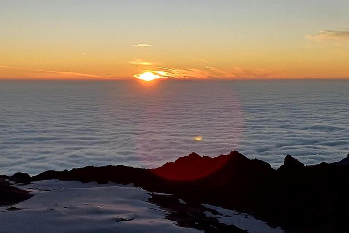 un apus de soare pe vârful unui munte, deasupra norilor