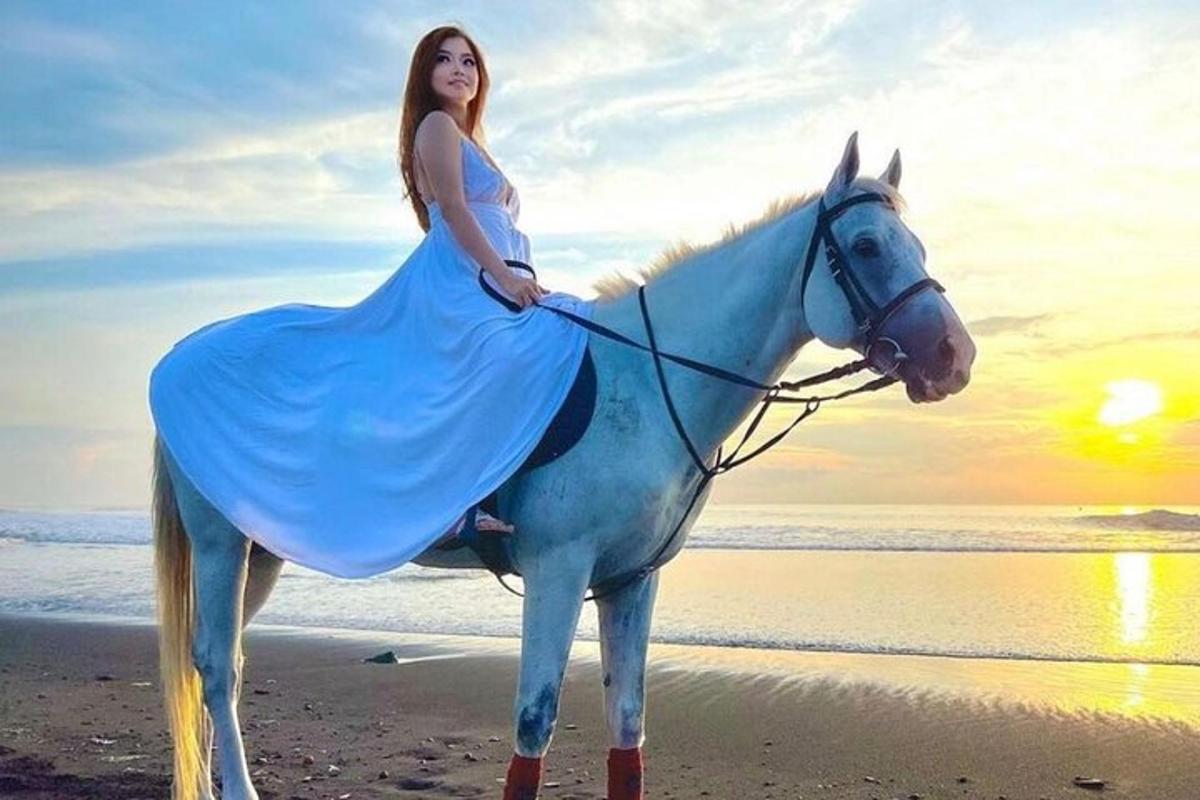 uma mulher de vestido cavalgando um cavalo na praia