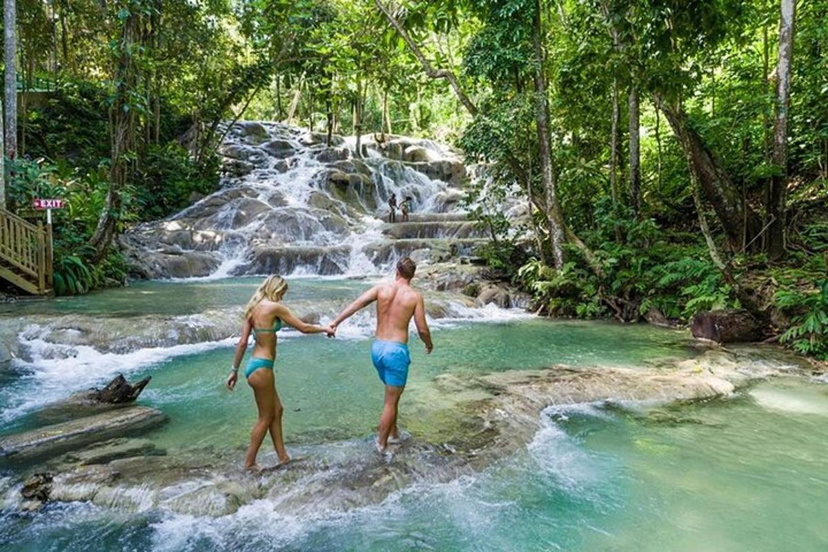 seorang lelaki dan wanita berdiri di dalam kolam air di hadapan air terjun
