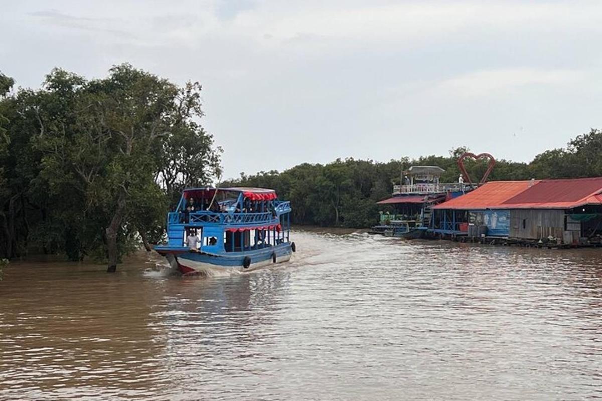 một chiếc thuyền màu xanh đang đi dọc theo một con sông bên cạnh những ngôi nhà