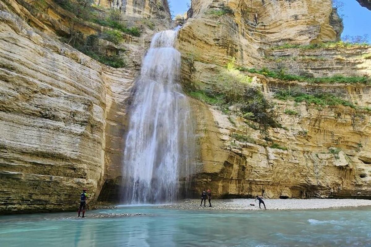 dua orang berdiri di dalam air berhampiran air terjun