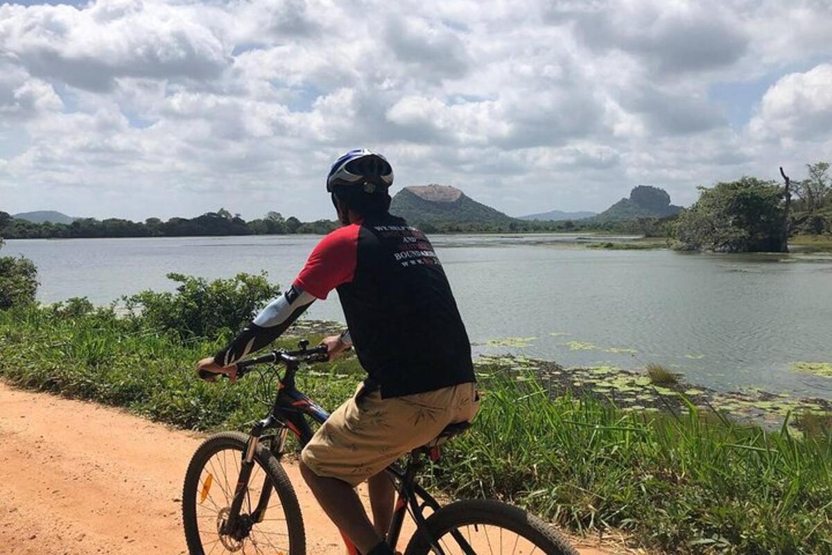 un home anant en bicicleta per un camí de terra al costat d'un riu