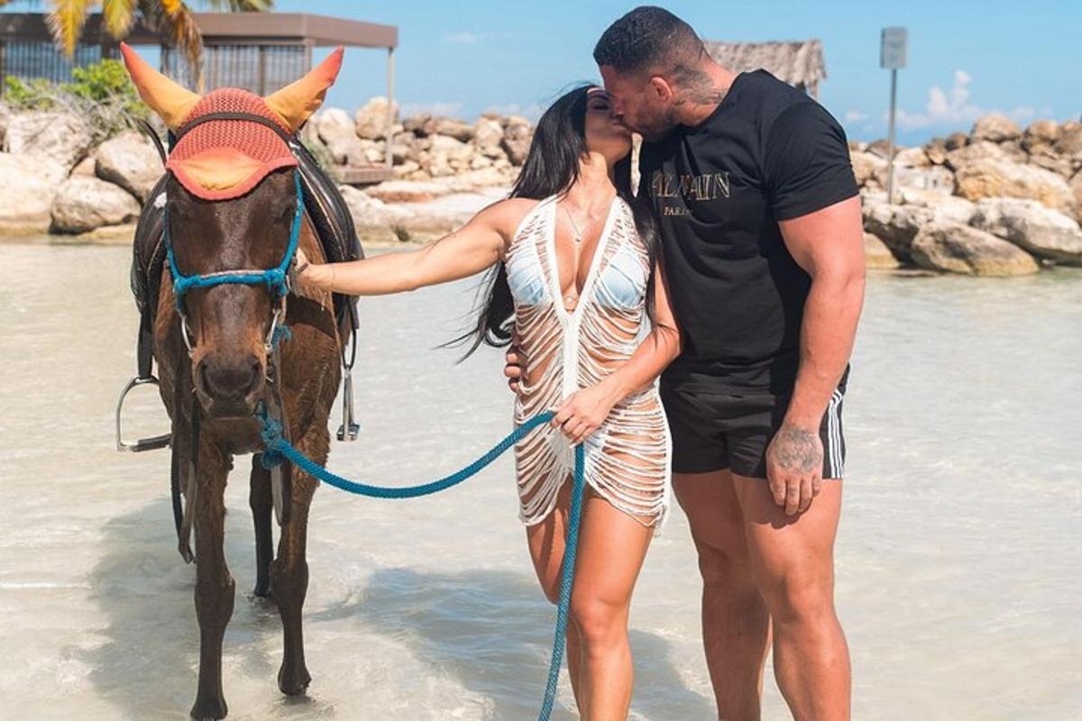 um homem e uma mulher em pé ao lado de um cavalo na praia