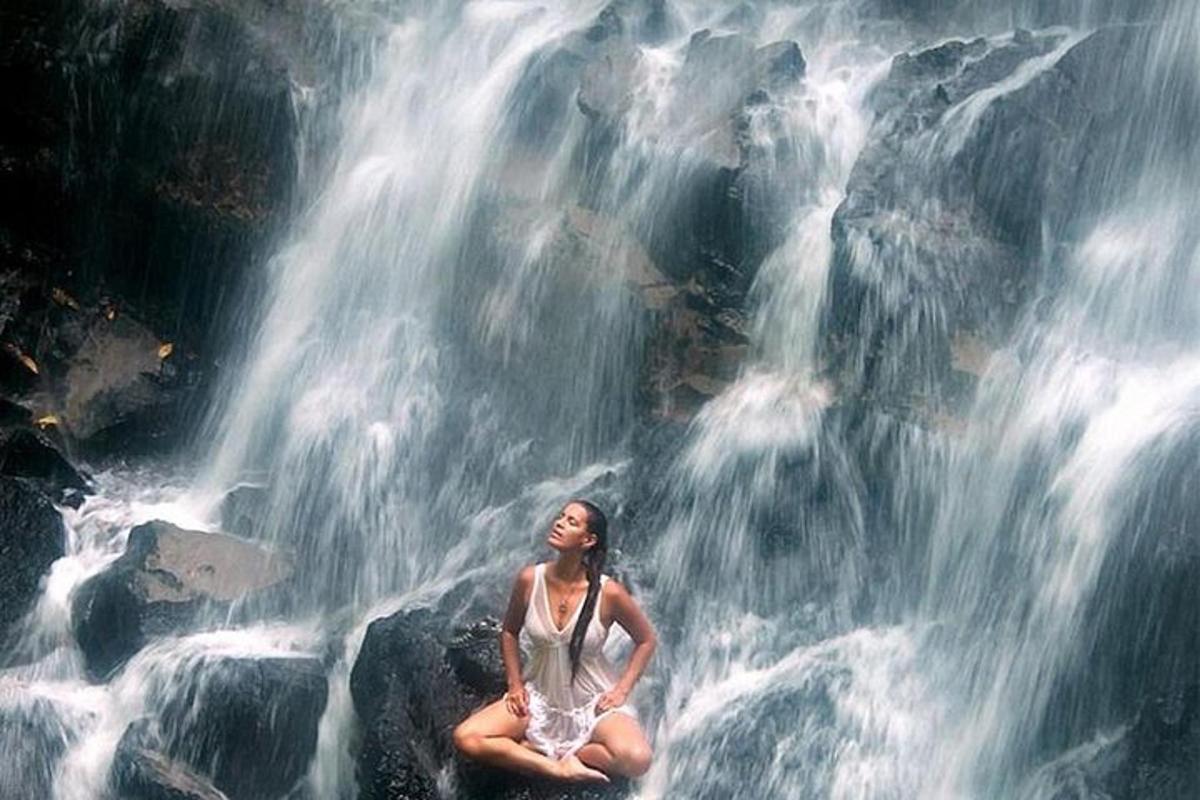 uma mulher sentada em uma rocha em frente a uma cachoeira