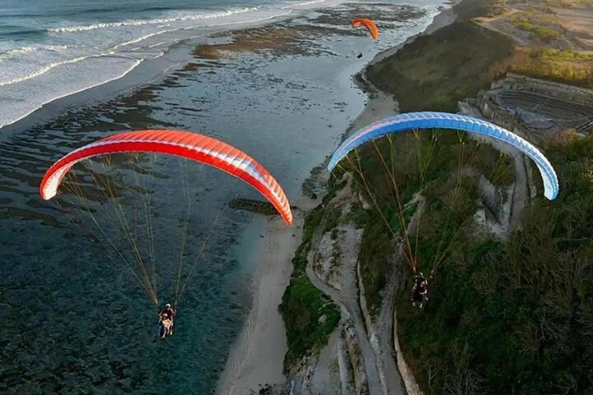 two people flying parachutes over the water near the beach