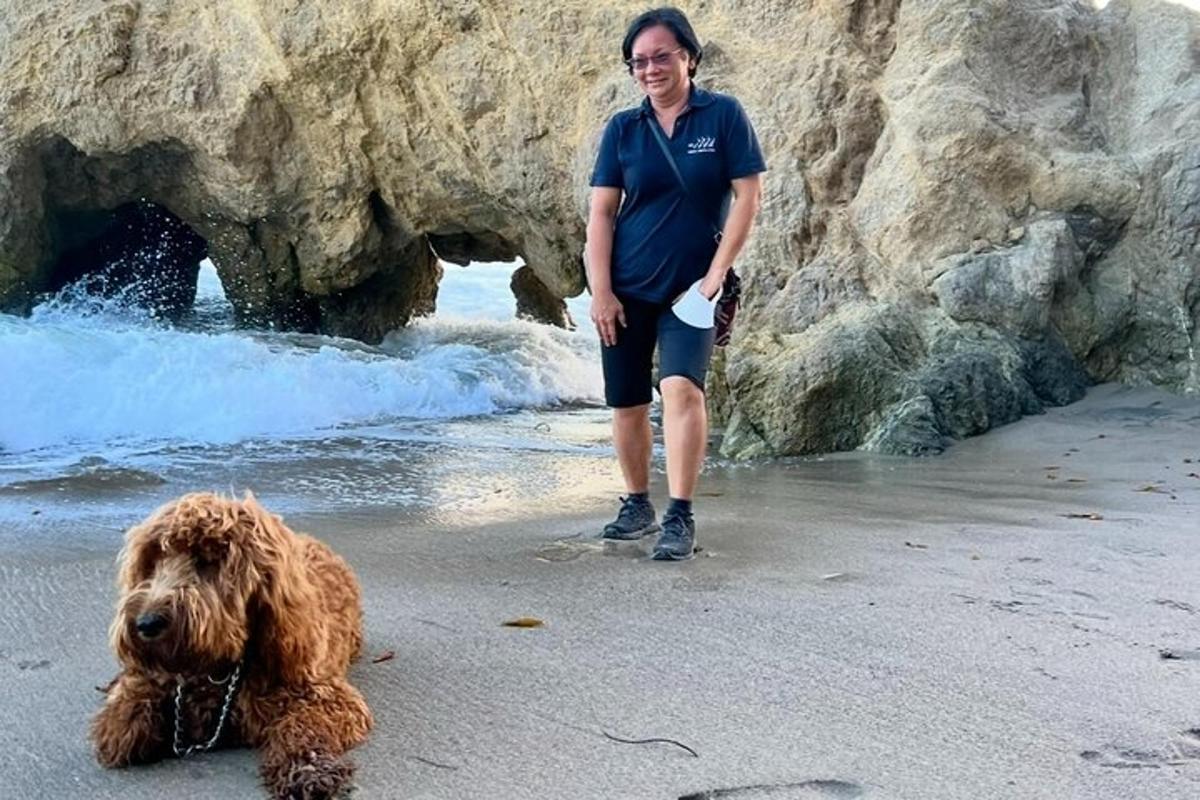 Una mujer parada junto a un perro en la playa