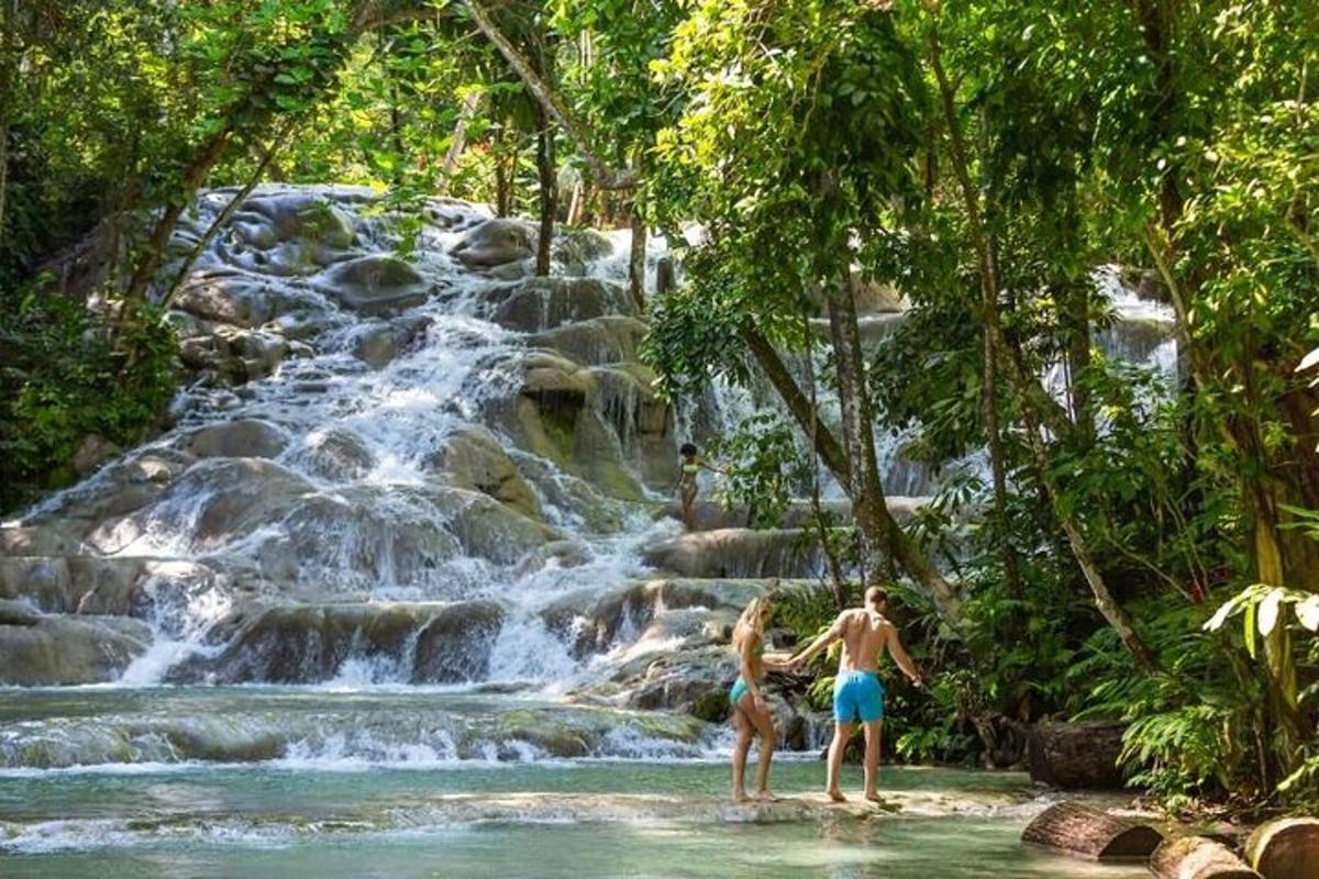dua orang berdiri di dalam air di hadapan air terjun