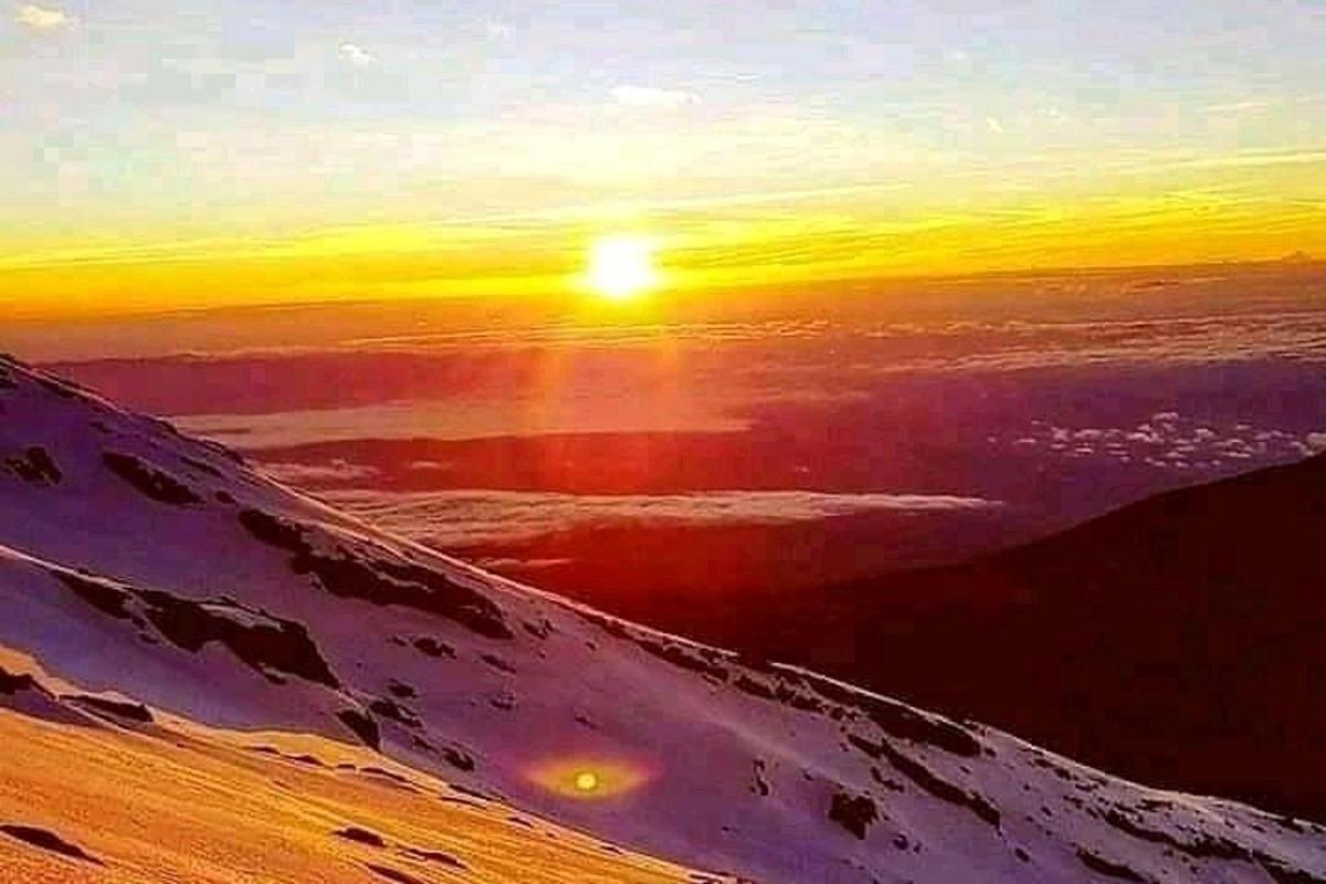 雪に覆われた山の頂上からの夕日