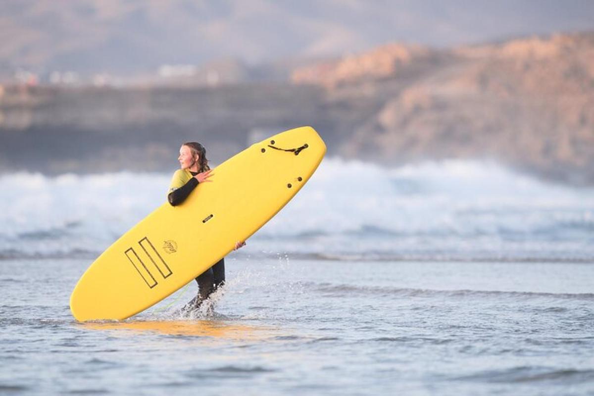 una persona sosteniendo una tabla de surf amarilla en el agua