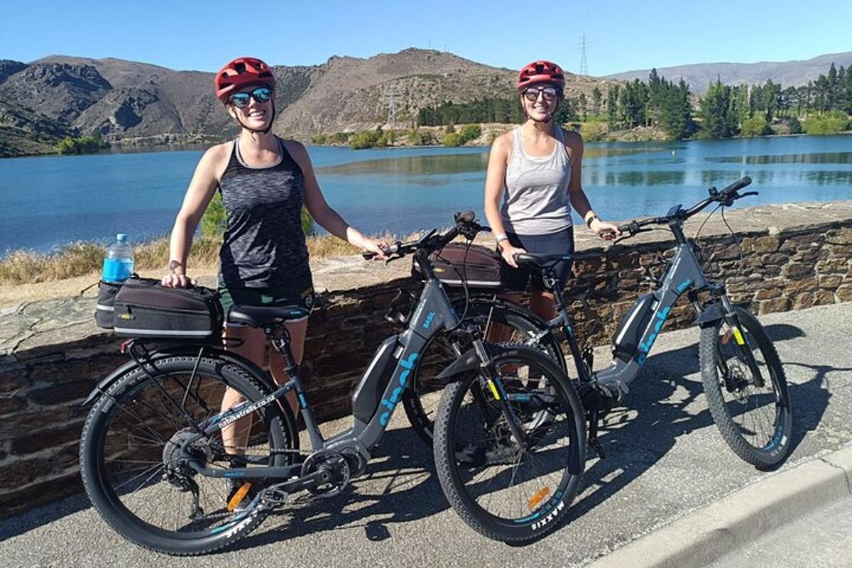 Dos mujeres paradas con sus bicicletas frente a un lago