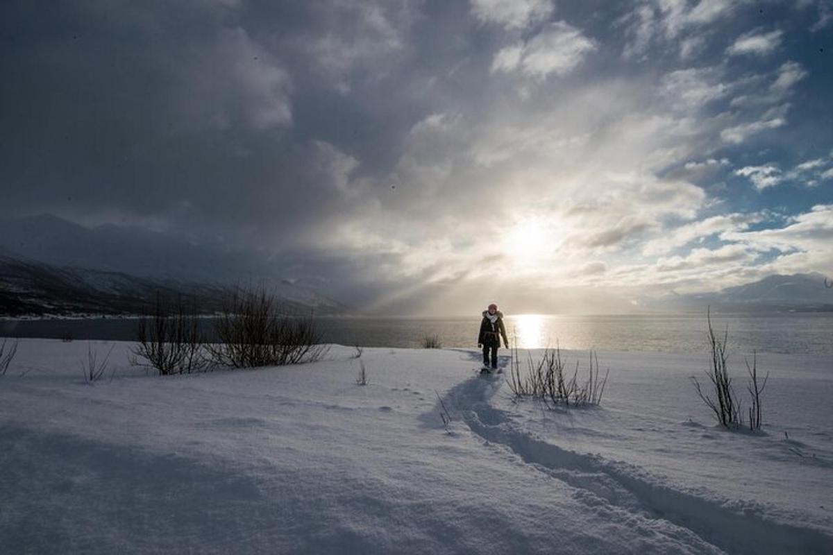 uma pessoa caminhando na neve com o sol ao fundo