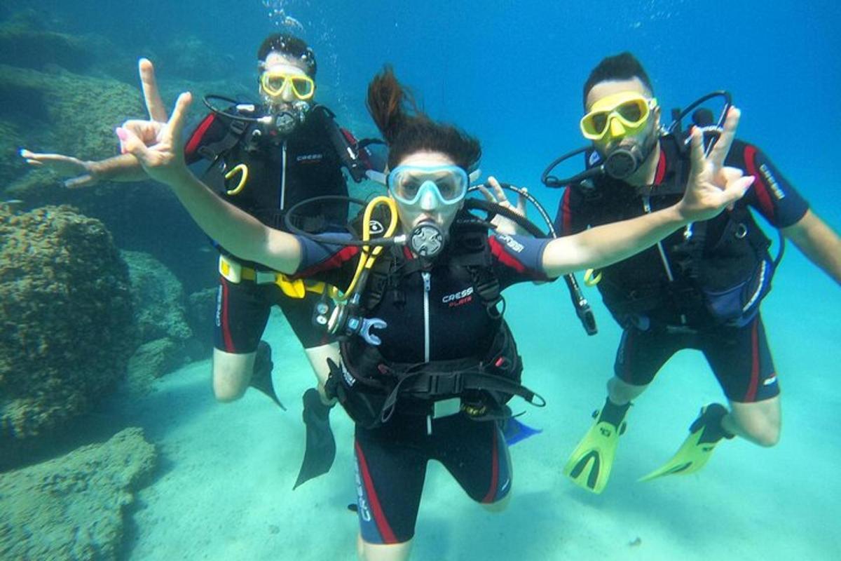 tiga orang dalam peralatan skuba berenang di dalam air