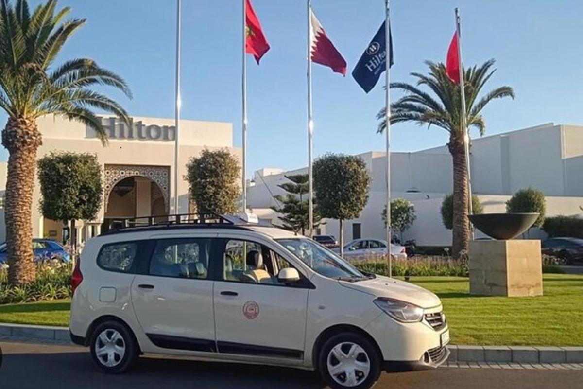 sebuah mobil putih terparkir di depan sebuah gedung dengan bendera